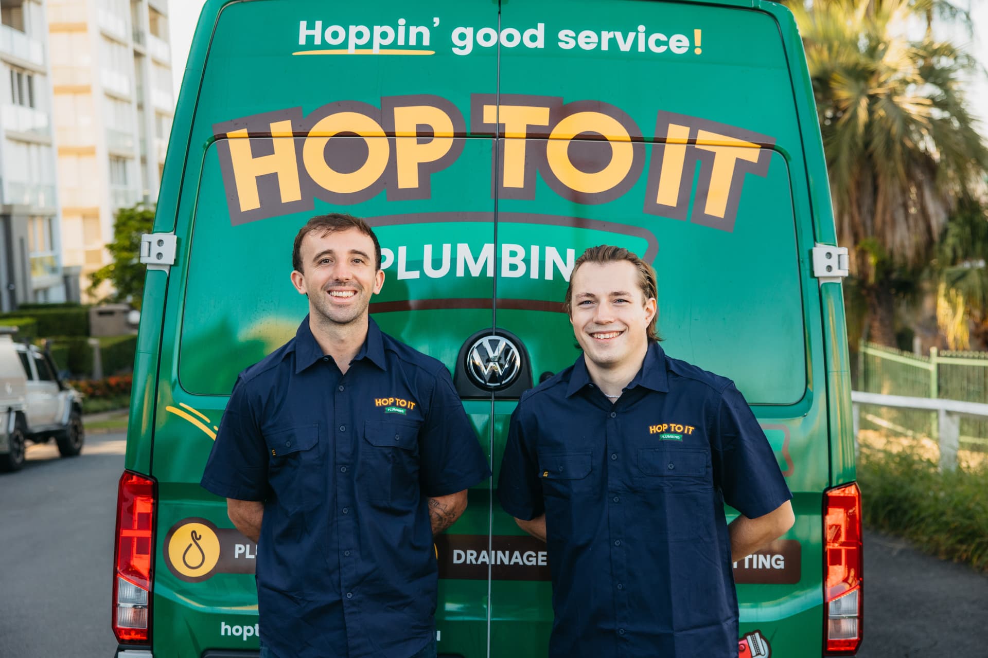 Two Hop To It plumbers standing in front of a branded Hop To It van